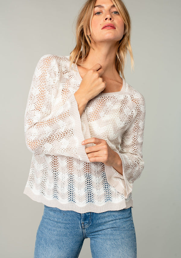 [Color: Linen/Ivory] A model wearing a beige and off white crochet knit sweater with bohemian long bell sleeves and a chevron knit pattern.