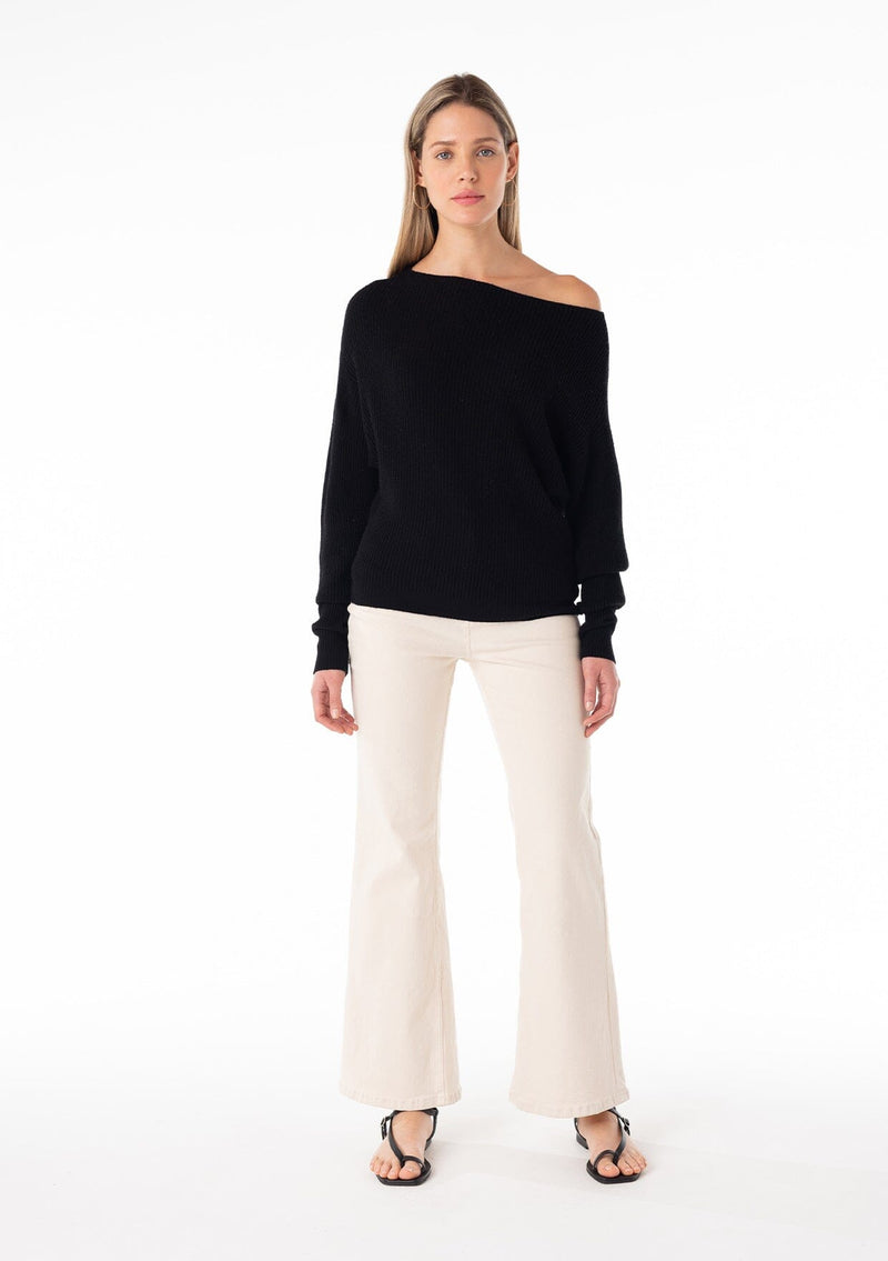 [Color: Black] A full body front facing image of a blonde model wearing a black waffle knit pullover sweater. With long sleeves, a relaxed fit, and a wide neckline that can be worn off the shoulder. 