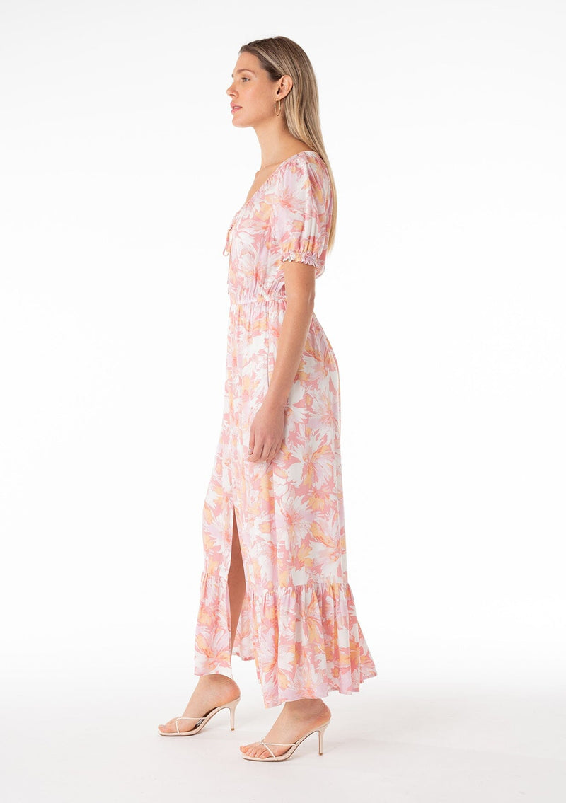 [Color: Peach/Light Pink] A side facing image of a blonde model wearing a classic spring bohemian maxi dress in a peach pink floral print. With short puff sleeves, a front slit, an elastic waist, and a drawstring v neckline with adjustable tie. 