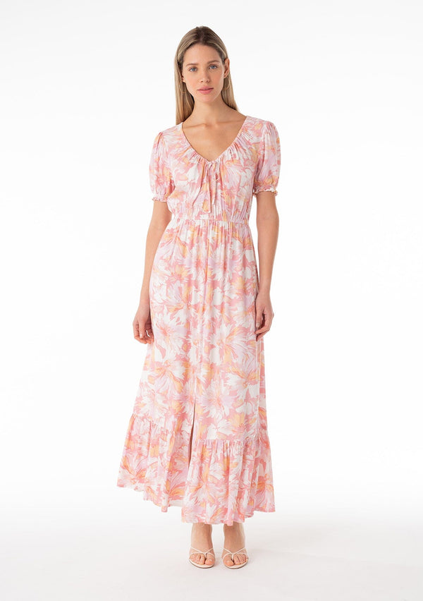 [Color: Peach/Light Pink] A front facing image of a blonde model wearing a classic spring bohemian maxi dress in a peach pink floral print. With short puff sleeves, a front slit, an elastic waist, and a drawstring v neckline with adjustable tie. 