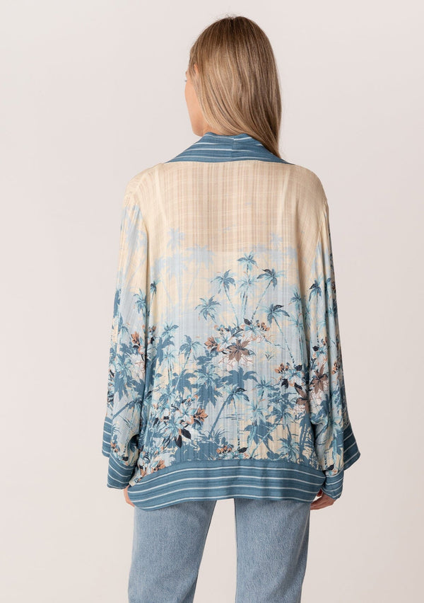 [Color: Blue/Natural] A back facing image of a blonde model wearing a bohemian kimono top in a blue floral print. With long flared sleeves, a relaxed flowy fit, and a tie front waist. 