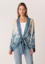 [Color: Blue/Natural] A front facing image of a blonde model wearing a bohemian kimono top in a blue floral print. With long flared sleeves, a relaxed flowy fit, and a tie front waist. 