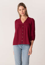 [Color: Merlot] A front facing image of a blonde model wearing a classic bohemian blouse in a burgundy red soft cotton gauze. With three quarter length puff sleeves, a v neckline, a button front, and embroidered details throughout. 