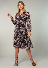 [Color: Black/Dusty Rose] A front facing image of a blonde model wearing a sheer chiffon mid length dress in a black and lavender purple floral print. With sheer long sleeves, a button front, a collared neckline, and a drawstring waist that can be adjusted to fit loose or defined. 