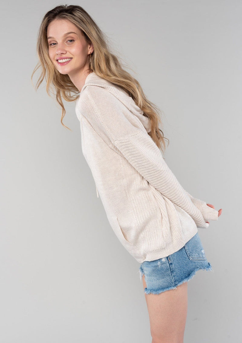 [Color: Vanilla] A blonde model wearing a cozy cream colored knit hoodie sweater with long sleeves and a front kangaroo pocket.