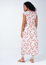 [Color: Natural/Rose] A back facing image of a brunette model wearing a cotton blend mid length spring dress in a natural and rose pink floral print. With short cap sleeves, a self covered button front, a v neckline, and sexy side waist cutouts.