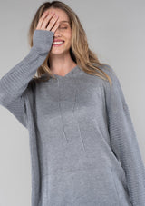 [Color: Heather Grey] A blonde model wearing a cozy heather grey knit hoodie sweater with long sleeves and a front kangaroo pocket. 