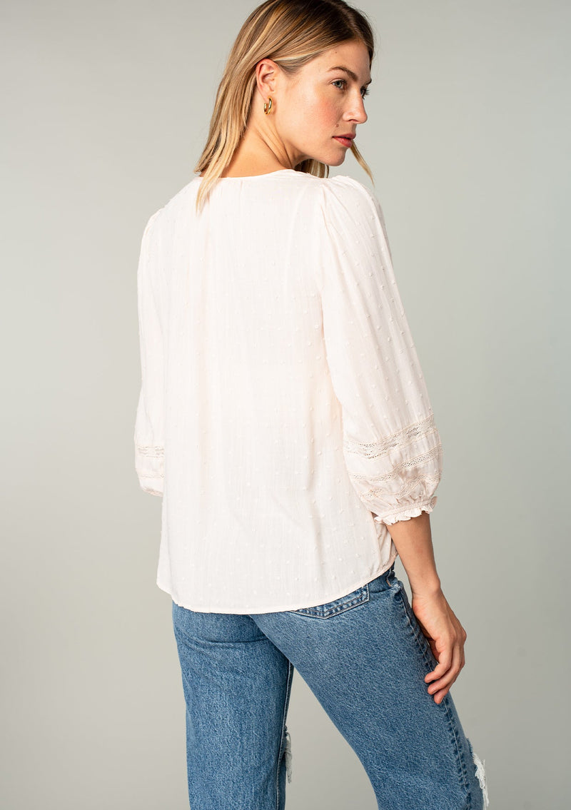 [Color: Almond] A back facing image of a blonde model wearing a light pink classic bohemian peasant top with voluminous lace trimmed long sleeves.