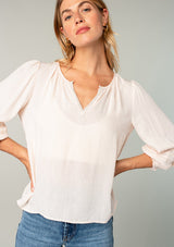 [Color: Almond] A close up front facing image of a blonde model wearing a light pink classic bohemian peasant top with voluminous lace trimmed long sleeves.