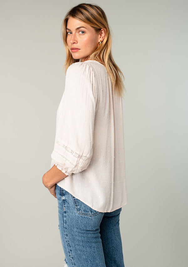 [Color: Almond] A side facing image of a blonde model wearing a light pink classic bohemian peasant top with voluminous lace trimmed long sleeves.