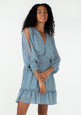 [Color: Dusty Blue/Natural] A front facing image of a brunette model wearing a sheer chiffon bohemian mini dress in an abstract squiggle print. With long billowy split sleeves, an open back with tassel tie closure, a smocked elastic waist, and a ruffle trimmed tiered skirt.