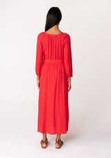 [Color: Red] A back facing image of a brunette model wearing a classic bright red bohemian maxi dress. With long sleeves, a round neckline, a button front, side pockets, and a self tie waist belt.