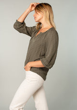 [Color: Olive] A side facing image of a blonde model wearing an olive green classic bohemian peasant top with voluminous lace trimmed long sleeves.