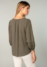 [Color: Olive] A back facing image of a blonde model wearing an olive green classic bohemian peasant top with voluminous lace trimmed long sleeves.