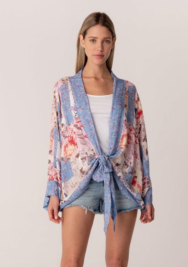 [Color: Natural/Periwinkle] A front facing image of a blonde model wearing a bohemian kimono top in a blue and pink floral print. With long flared sleeves, a relaxed flowy fit, and a tie front waist. 
