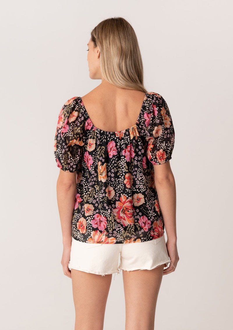 [Color: Black/Fuchsia] A back facing image of a blonde model wearing a bohemian spring top in a black and pink floral print. With short puff sleeves, a square neckline, and a relaxed fit. 