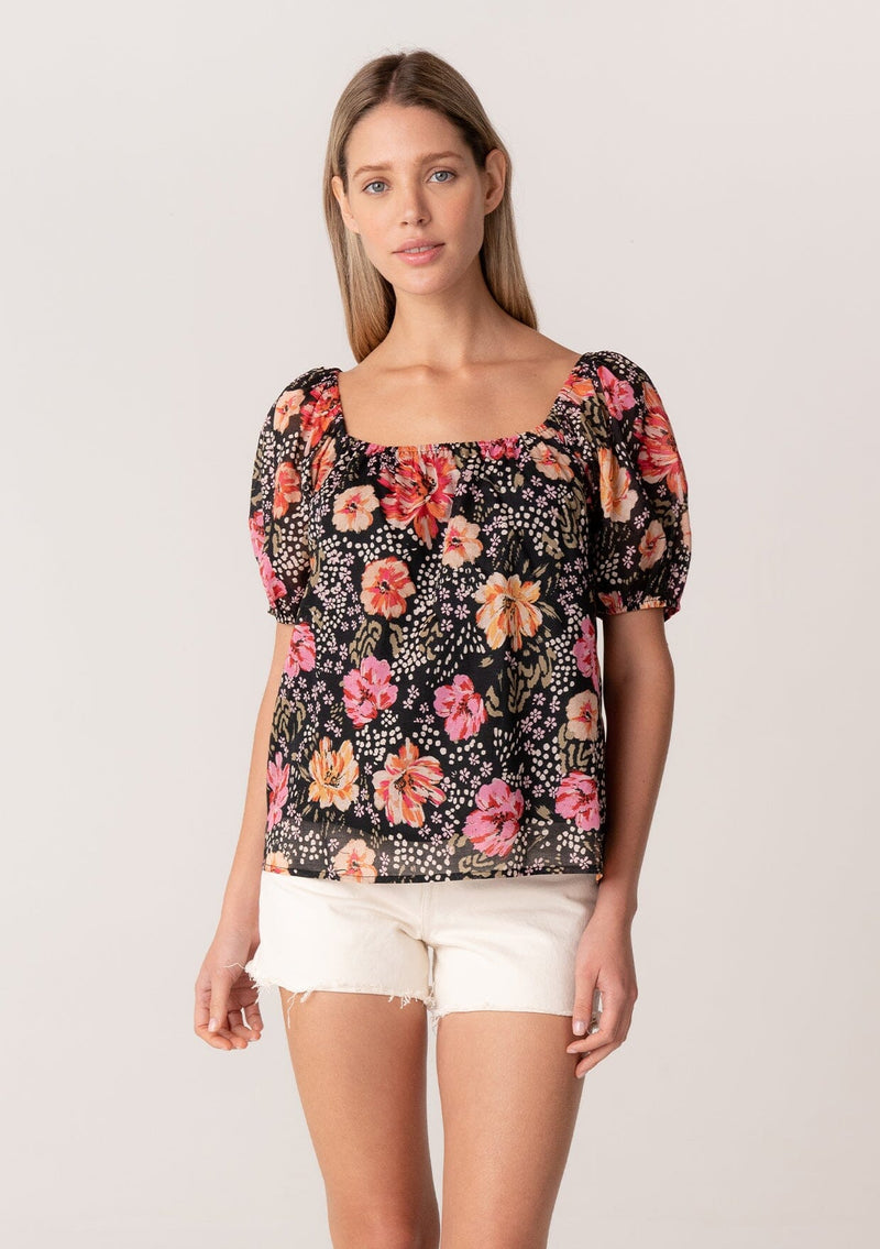 [Color: Black/Fuchsia] A front facing image of a blonde model wearing a bohemian spring top in a black and pink floral print. With short puff sleeves, a square neckline, and a relaxed fit. 