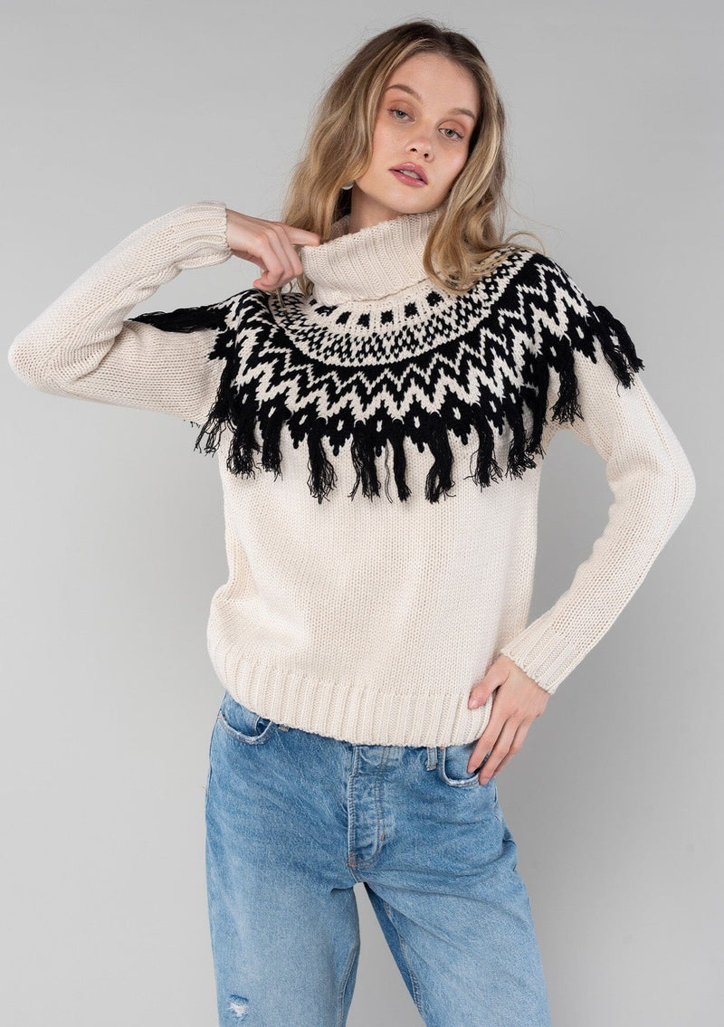 [Color: Ivory/Black] A cozy ski sweater with a bohemian twist. Featuring a warm turtleneck and a contrast knit yoke design and a fringed detail in front and back.