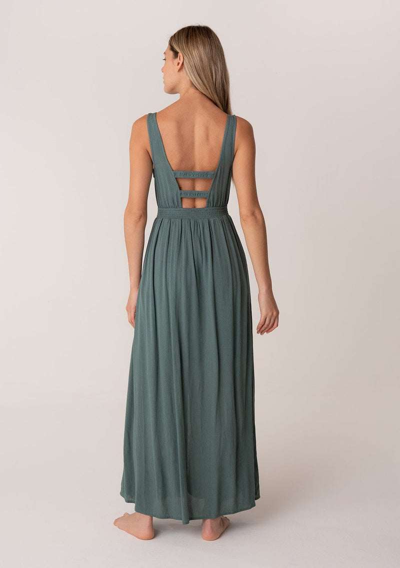 [Color: Lagoon] A back facing image of a blonde model wearing a bohemian sleeveless spring maxi dress in dusty teal. With a self covered button front, a deep v neckline, a front slit, a smocked elastic empire waist, and an open back with elastic strap detail.