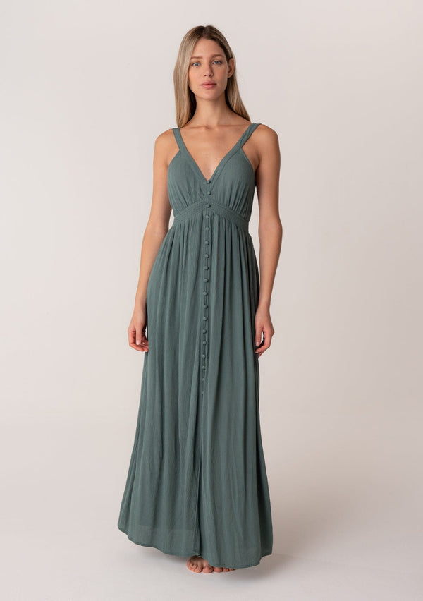 [Color: Lagoon] A front facing image of a blonde model wearing a bohemian sleeveless spring maxi dress in dusty teal. With a self covered button front, a deep v neckline, a front slit, a smocked elastic empire waist, and an open back with elastic strap detail.