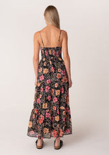 [Color: Black/Fuchsia] A back facing image of a blonde model wearing a pretty spring maxi dress in a black and pink floral print. With spaghetti straps, a scooped neckline, a flowy tiered skirt, a button front, and a half smocked elastic bodice at the back. 