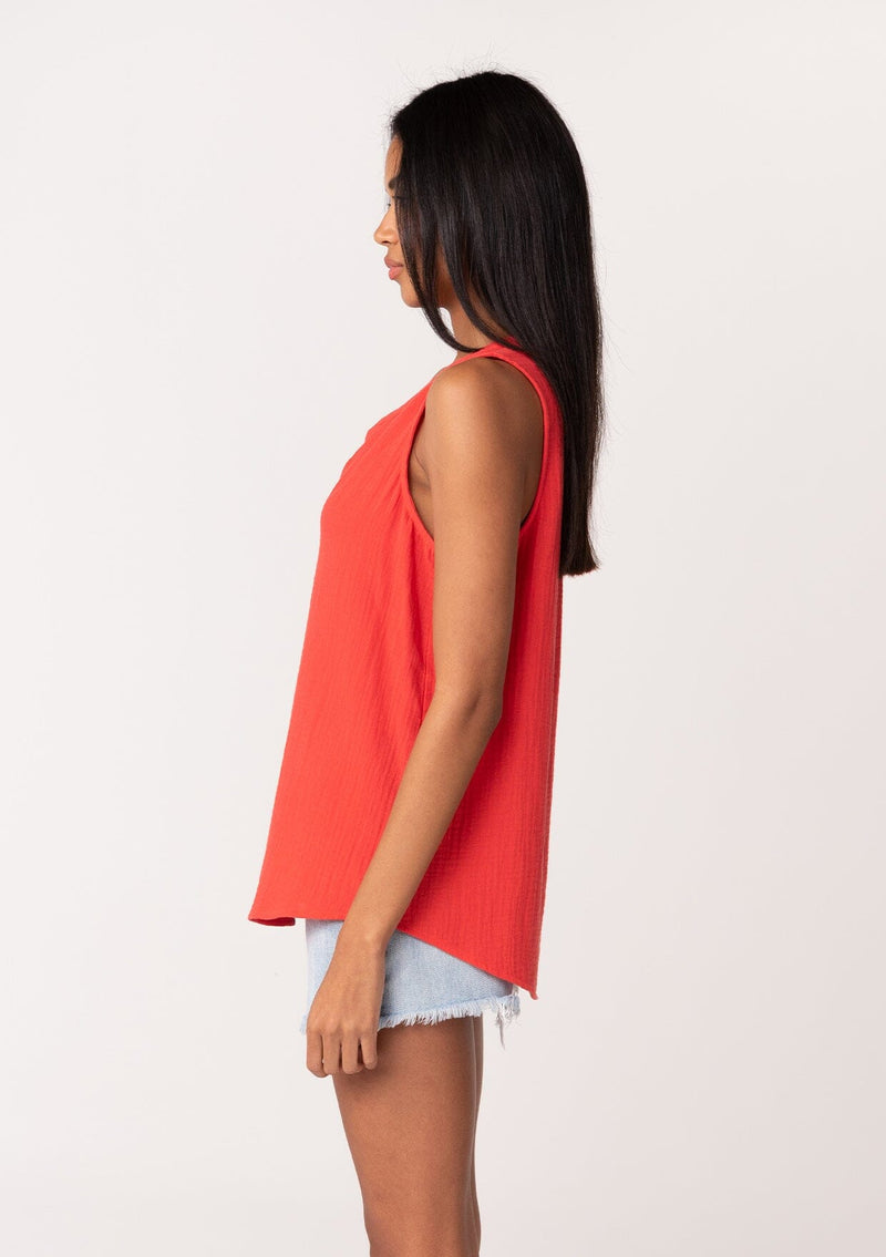 [Color: Flame] A side facing image of a brunette model wearing a simple bright red cotton tank top with a button front, a v neckline, and a relaxed fit. 