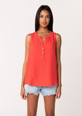 [Color: Flame] A front facing image of a brunette model wearing a simple bright red cotton tank top with a button front, a v neckline, and a relaxed fit. 