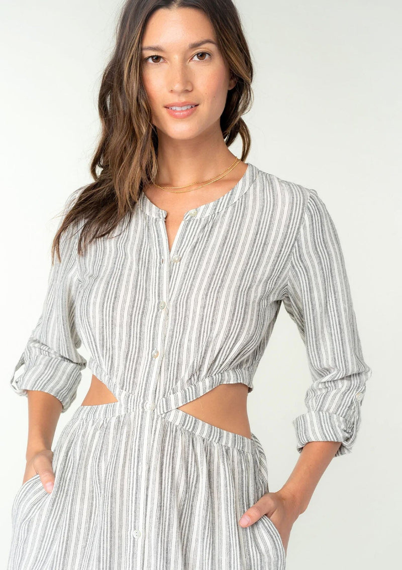 [Color: White/Black] A back facing image of a brunette model wearing a striped black and white cotton blend mid length shirt dress. With long rolled sleeves, a button front, a round neckline, side pockets, and sexy side waist cutout details. 