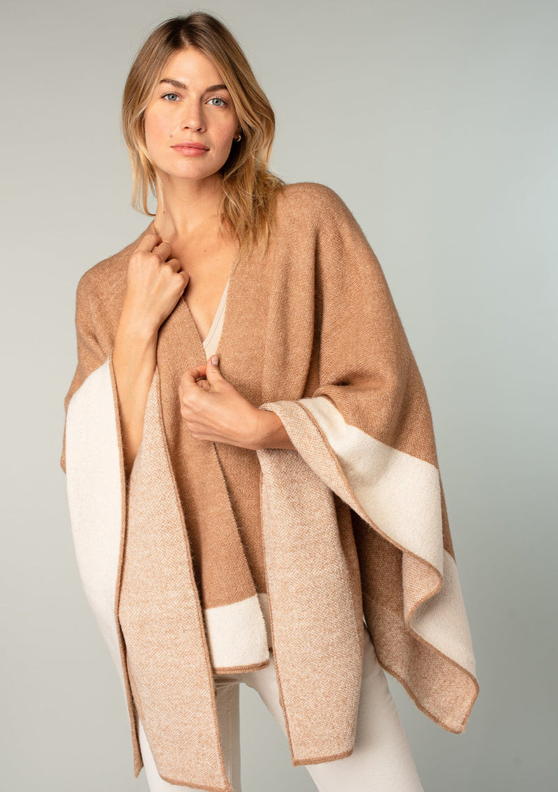 [Color: Heather Camel/Heather Ivory] A front facing image of a blonde model wearing a soft and warm mid length sweater cape. An open front cape cardigan with a contrast border design. Perfect fall sweater, great for layering. 