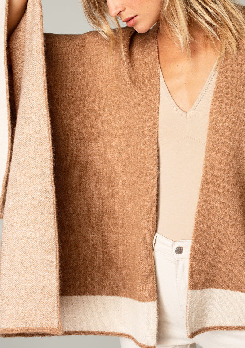 [Color: Heather Camel/Heather Ivory] A close up front facing image of a blonde model wearing a soft and warm mid length sweater cape. An open front cape cardigan with a contrast border design. Perfect fall sweater, great for layering. 