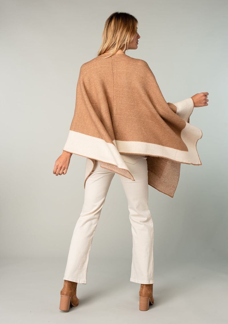 [Color: Heather Camel/Heather Ivory] A back facing image of a blonde model wearing a soft and warm mid length sweater cape. An open front cape cardigan with a contrast border design. Perfect fall sweater, great for layering. 