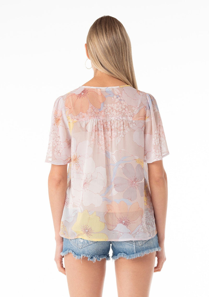 [Color: Natural/Blue] A back facing image of a blonde model wearing a pretty spring chiffon blouse designed in a pink and blue floral print. With short flutter sleeves, a split v neckline with ties, and a relaxed flowy fit. 
