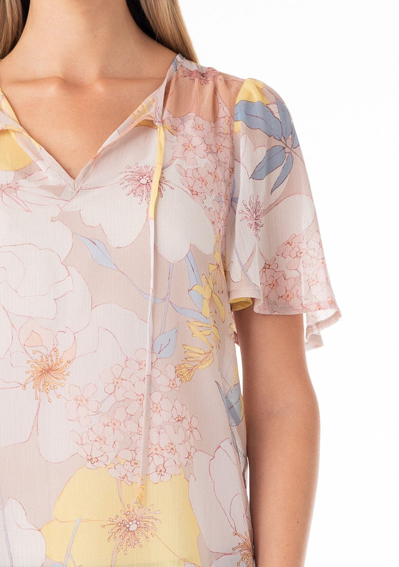 [Color: Natural/Blue] A close up front facing image of a blonde model wearing a pretty spring chiffon blouse designed in a pink and blue floral print. With short flutter sleeves, a split v neckline with ties, and a relaxed flowy fit. 
