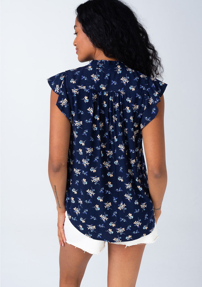 [Color: Navy/Coral] A back facing image of a brunette model wearing a classic bohemian button front top in a navy blue and coral floral print. With short flutter cap sleeves and a ruffled neckline. 