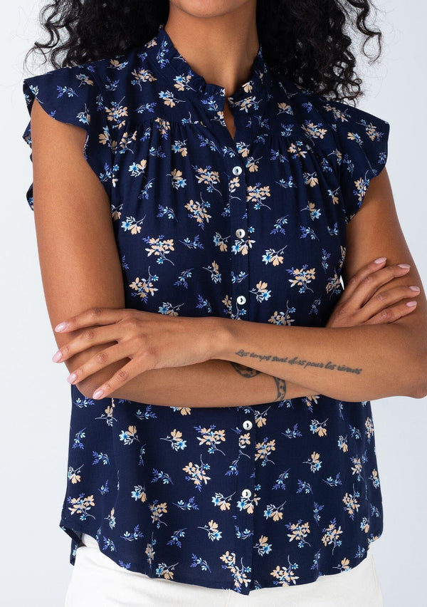 [Color: Navy/Coral] A close up front facing image of a brunette model wearing a classic bohemian button front top in a navy blue and coral floral print. With short flutter cap sleeves and a ruffled neckline. 