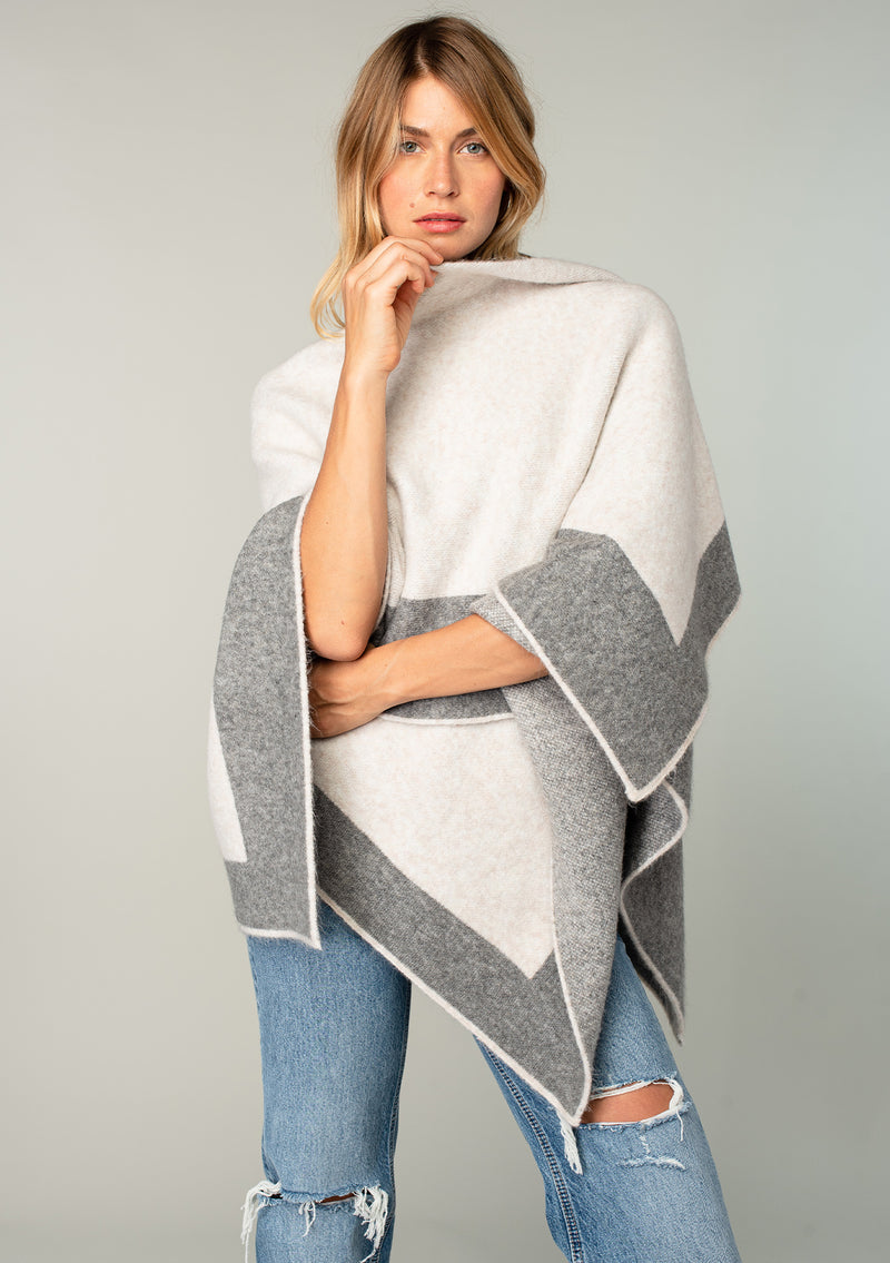 [Color: Heather Natural/Heather Grey] A front facing image of a blonde model wearing a soft and warm mid length sweater cape. An open front cape cardigan with a contrast border design. Perfect fall sweater, great for layering. 
