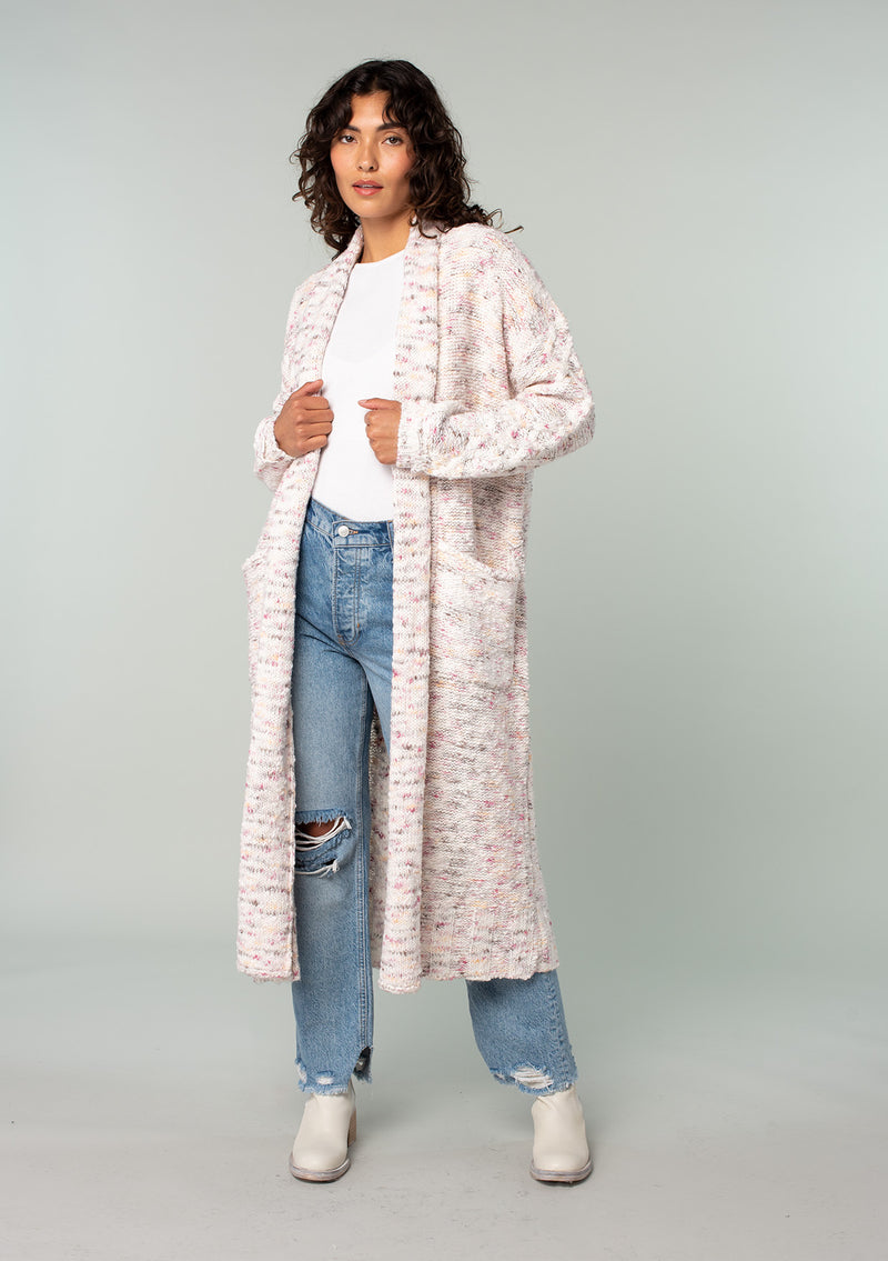 [Color: Natural/Berry] A front facing image of a brunette model wearing a natural off white and berry speckled knit long cardigan with an open front, side pockets, and cable knit details. 