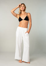 [Color: White] A full body front facing image of a blonde model wearing a white boho relaxed fit beach pant in cotton gauze. With a wide leg, side pockets, and a smocked elastic waistband.