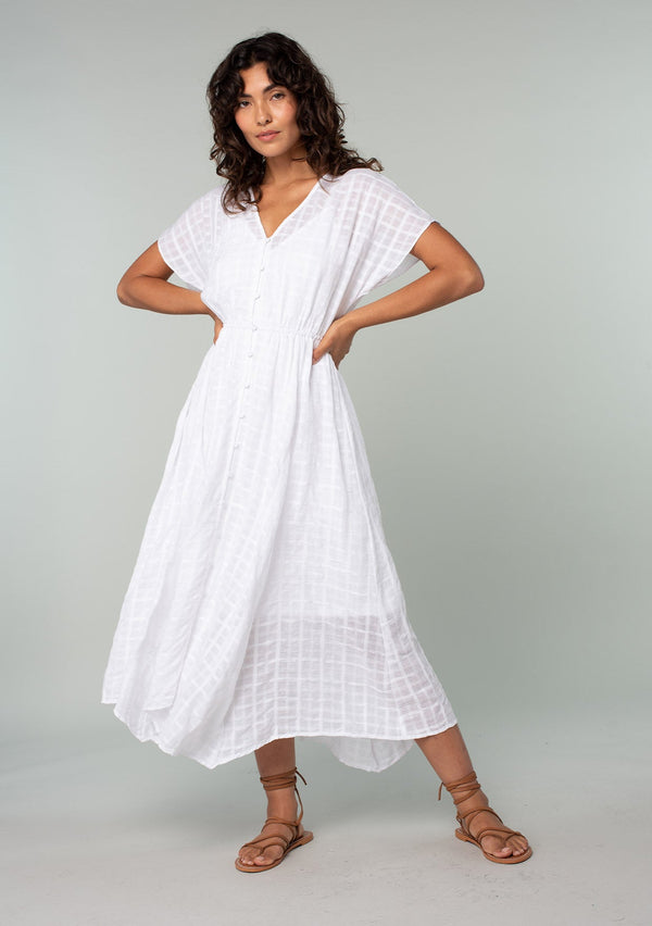 [Color: White] A full body front facing image of a brunette model with wearing a white cotton button front maxi dress with short sleeves and an allover textured gingham.