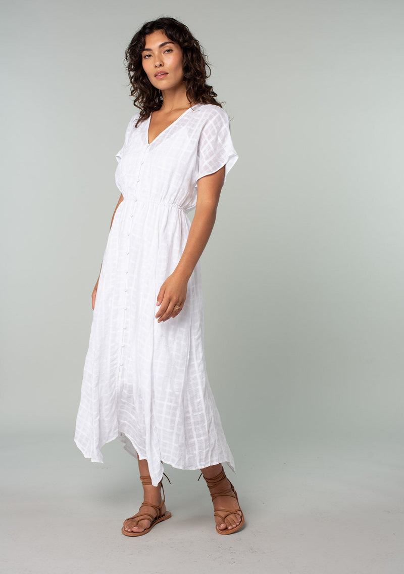 [Color: White] A full body side facing image of a brunette model with wearing a white cotton button front maxi dress with short sleeves and an allover textured gingham.