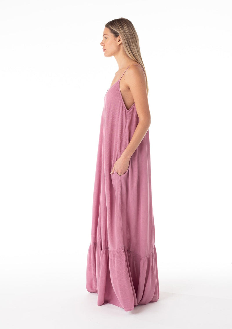 [Color: Smokey Orchid] A side facing image of a blonde model wearing a simple flowy sleeveless maxi tank dress in a light purple crinkle rayon. With a v neckline in front and back, adjustable spaghetti straps, and a tiered skirt. 