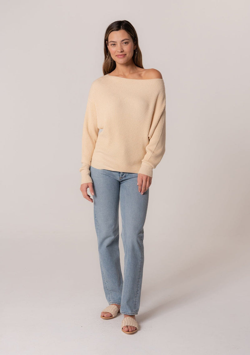 [Color: Cream] A full body front facing image of a brunette model wearing a cream waffle knit pullover sweater. With long sleeves, a relaxed fit, and a wide neckline that can be worn off the shoulder.