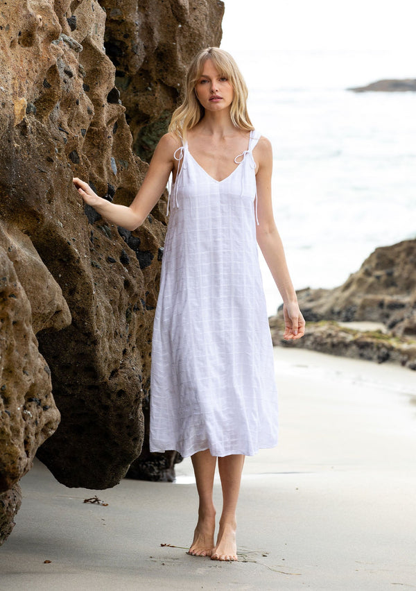 [Color: White] A model wearing a bohemian cotton white mid length dress with tank top straps and a v neckline in front and back. 