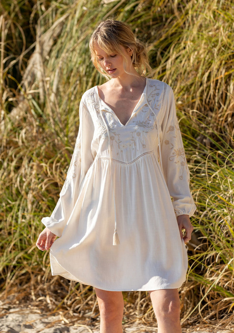 [Color: Vanilla/Sand] A model wearing a bohemian off white mini dress with embroidered detail.