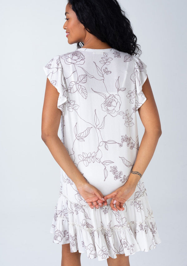 [Color: Natural/Taupe] A back facing image of a brunette model wearing a bohemian spring mini dress in an off white and taupe floral print. With short flutter sleeves, a button front, a ruffle trimmed tiered skirt, and a loose relaxed fit. 