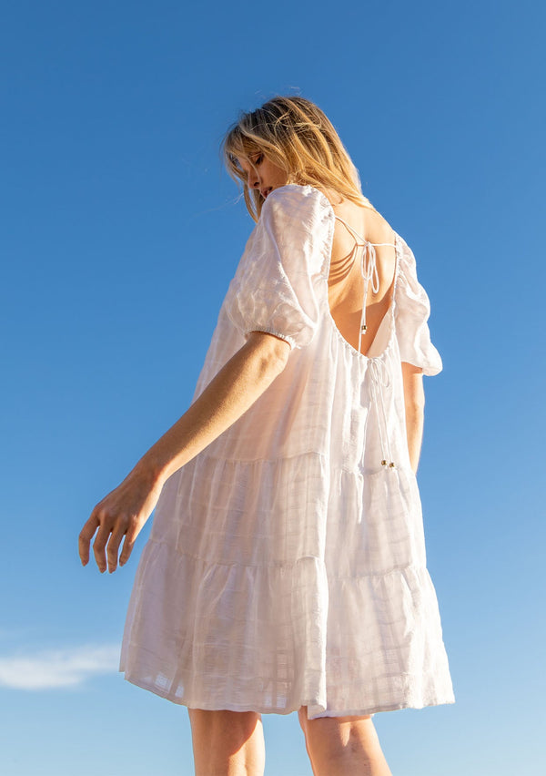 [Color: White] A model wearing a bohemian white cotton mini dress with short puff sleeves and a relaxed flowy fit.