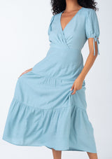 [Color: Dusty Blue] A close up front facing image of a bohemian dusty blue mid length dress. With short puff sleeves, adjustable tie cuffs, a flowy tiered skirt, and a surplice v neckline. 