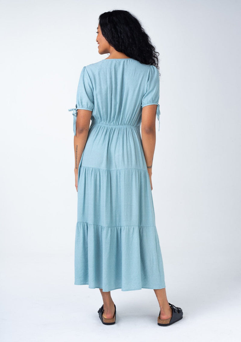 [Color: Dusty Blue] A back facing image of a bohemian dusty blue mid length dress. With short puff sleeves, adjustable tie cuffs, a flowy tiered skirt, and a surplice v neckline. 