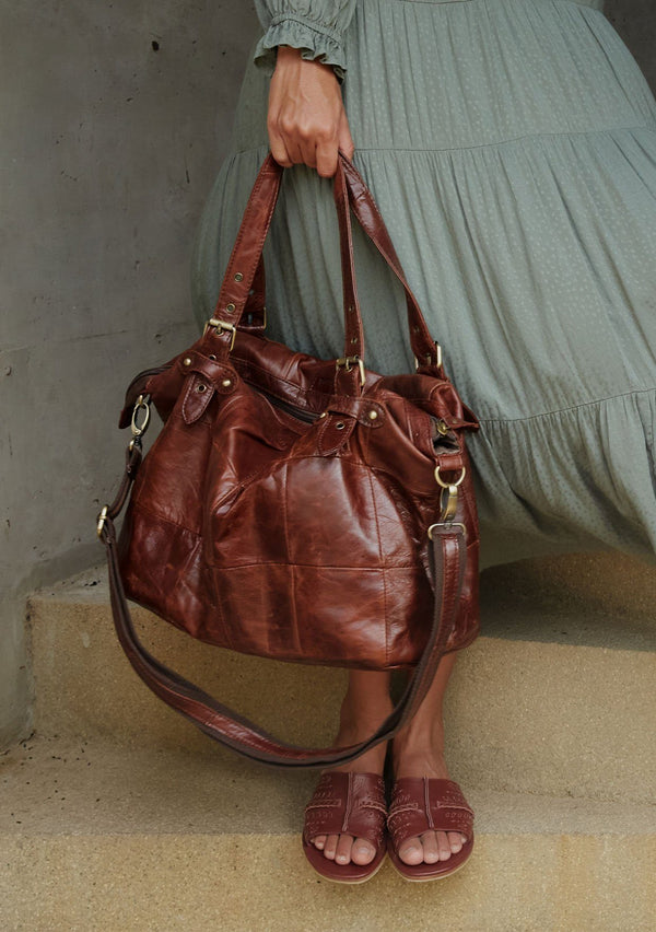 [Color: Brown] A brown quilted leather bag with buckled handles, a removable long strap, a zippered closure, and a center zippered interior compartment.