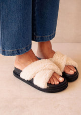 [Color: Black] Alohas cozy slipper cloud black sandals. Featuring a double layered chunky sole and white criss crossed straps made of fluffy natural shearling.
